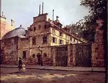 A large imposing house with solid beige walls and small windows, connected to a parallel wall, looms over an empty street.