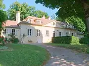 Photo of a light yellow house with shuttered windows, surrounded by trees and shrubs