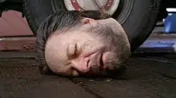 A severed head lies on the floor, facing the viewer.