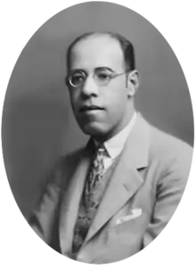 Photograph showing the head and shoulders of de Andrade with glasses wearing a suit