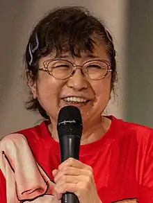 Mayumi Tanaka holding a microphone and smiling