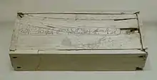 White rectangular box with small cracks and a long line of hieroglyphs along the entire length of the lid, at its centre