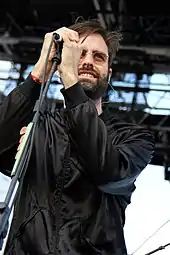 A man in a black jacket holding a microphone on stage.