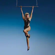 Miley Cyrus wearing a black one-piece swimsuit hanging from a helicopter ladder.