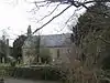 Stone building partially obscured by trees. In the foreground are gravestones.