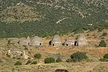 An image depicting 5 brick kilns with small entrances, two of the kilins have collapsed. It is surround by arid vegetation and mountains.