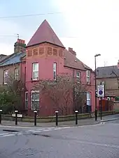 A brightly painted red house with a tall pointed tower, situated on a crossroads