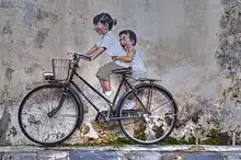 A mural depicting two children riding a bicycle.