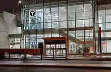 Photo of a glass station building with an entryway at ground level. An elevator and staircase are visible inside.