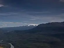 A glaciated, flat-topped, gently-sloping mountain with a much lower barren mountain in the right foreground.