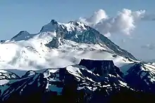 A rocky mountain with heavily glaciated lower slopes rising over a rocky ridge in the foreground.