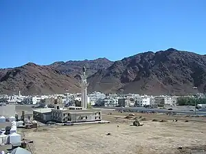 Black mountains in a desert with a white mosque with a minaret in the foreground