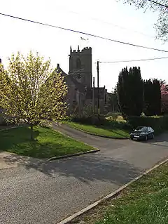 Stone building with square tower. In the foreground is a road.