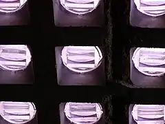 View from below of small circular panes of translucent lavender glass, deeply set in a coffered grid. Each circle has three parallel pendant-prism ridges.