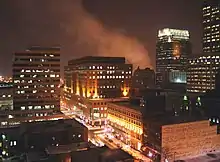 A landscape image of a city setting at night including several skyscrapers and a roadway illuminated by streetlights