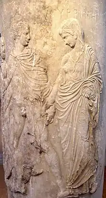 A carving of a noble robed man and woman apparently leading a demure robed woman. The man's robe is open, exposing his penis. He holds the hand of the woman.