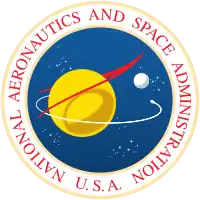 A blue sphere with stars, a yellow planet with a white moon; a red chevron representing wings, and an orbiting spacecraft; surrounded by a white border with "NATIONAL AERONAUTICS AND SPACE ADMINISTRATION U.S.A." in red letters