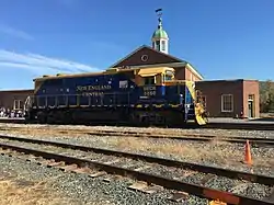 A blue and yellow diesel locomotive parked on railroad tracks, in front of a building