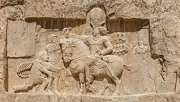 a relief cut into rocks depicting a man on horseback and two men, one standing and the other bowing in front of the horse rider