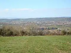 lots of house roofs, with trees and grass in the foreground and hills in the distance.