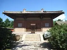 The Great Buddha Hall of Nanchan Temple. A small timber building with massive overhanging eaves with a bright blue sky behind it.