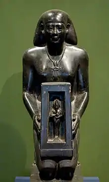 Statue of a kneeling man holding a box containing a small male figure