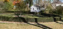 One-room wooden building; in foreground, circular hedge about 100 feet in diameter