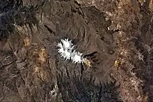 A roughly pear-shaped ice area, from which valleys emanate, lies within a multicolored landscape, as seen from a satellite image.