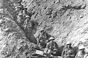 A black and white photograph of men in military uniform standing in a trench on a battlefield and looking at the camera