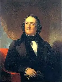 A stocky black-haired man with a white shirt, black bow-tie, and black suit