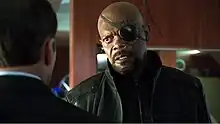 Man with an eye patch over his left eye talking to another man, in an over the shoulder shot