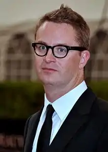 A photograph of filmmaker Nicholas Winding Refn, wearing glasses and suit with bow tie.