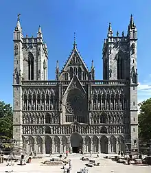 A Romanesque church with Gothic pointed arches. Two rectangular towers separated by a pitched roof entrance hall. The ornate facade is heavily articulated with repeated arches, most of them framing statues.