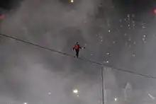 A man on a tightrope with mist and lights in the background