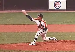 A man in a white baseball jersey with "ASTROS" on the chest and orange and yellow stripes on his shoulders pitches a baseball with his right hand.