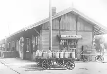 Norwalk, CA depot with deep eaves, loading docks and storefronts. A wagon, fully laden with milk cans is in front.