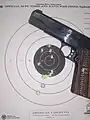 Handgun and paper target showing grouping of ten shots