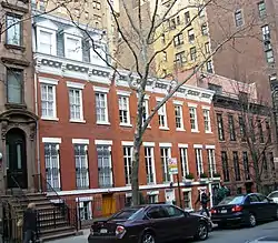 A row of five three-story brick townhouses. Three on the left have white trim, the other two black. There is roof on the one at the left.