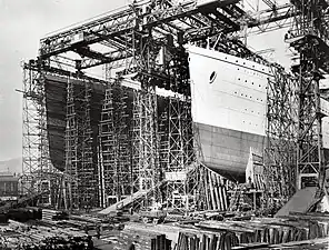 Photograph of a huge gantry with two openings in it, one of which is filled with the bows of a large ship that has been painted in light and dark colours.