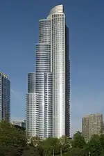 tall silver skyscraper with blue sky background beyond tall trees