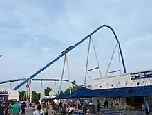 A blue roller coaster's first drop, with a 8 car train about to go down it.