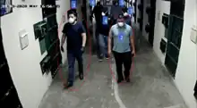 A screenshot of video surveillance footage showing various men waring face masks inside a prison hallway