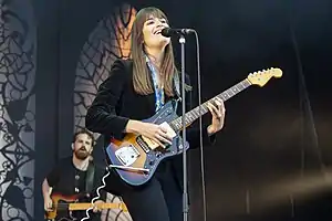 Clara Luciani performing onstage, holding a guitar and singing into a microphone