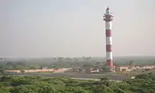 lighthouse with small houses and greenery in the background