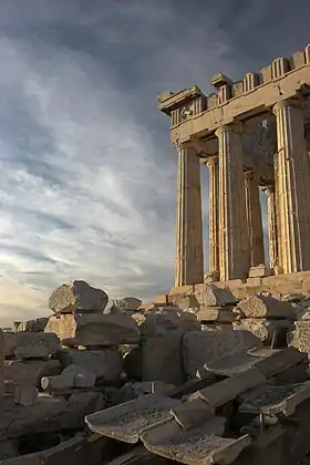 The Parthenon from the south. In the foreground of the image, a reconstruction of the marble imbrices and tegulae forming the roof is visible, resting on wooden supports.