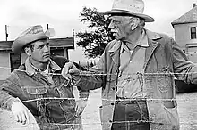 Younger man and older man, leaning on a barbed-wire fence and looking at each other