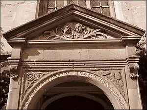 Part of a stone doorway. The top is triangular, with the heads of two cherubs in the panel beneath. On the curved arch immediately above the entrance, the words "Ascendat oratio descendat Gratia"; a rose and a thistle on the adjoining panels