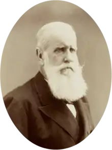 Half-length photographic portrait of an older man with white hair and beard dressed in a dark jacket and necktie