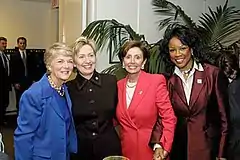 Four adult women standing in a lobby perhaps, stiff pose, large indoor plant in background