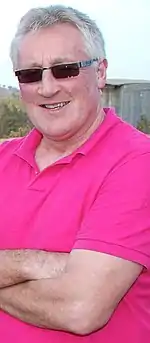 A smiling grey-haired man in a pink shirt and sunglasses